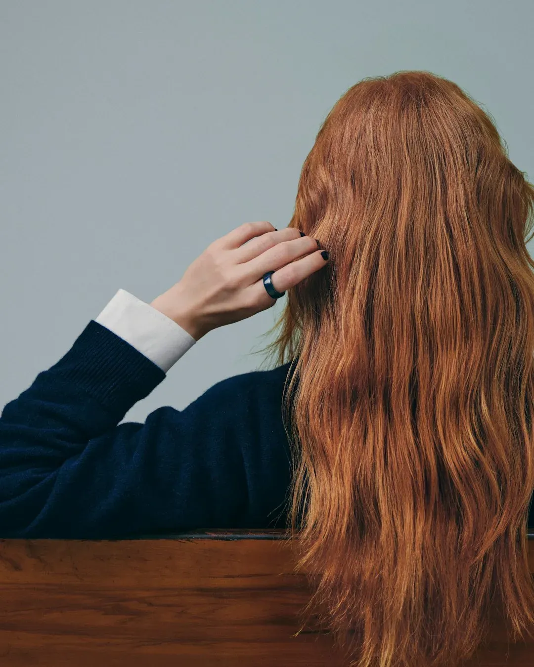 Une femme de dos, la main dans les cheveux, l'Oura Ring 4 Ceramic Midnight au majeur