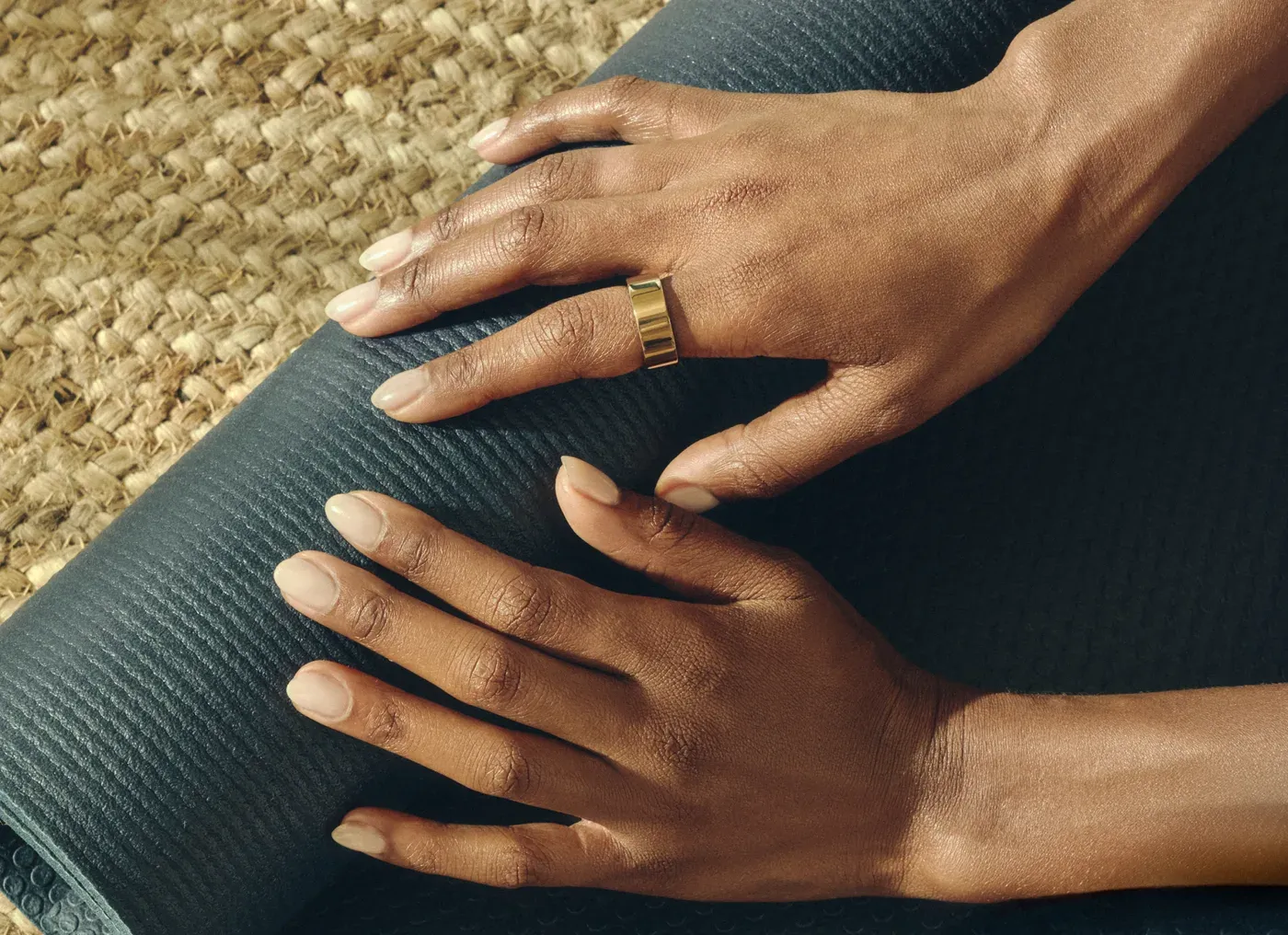 Ultrahuman Ring Air dorée portée à l'index, deux mains posées sur un tapis de yoga