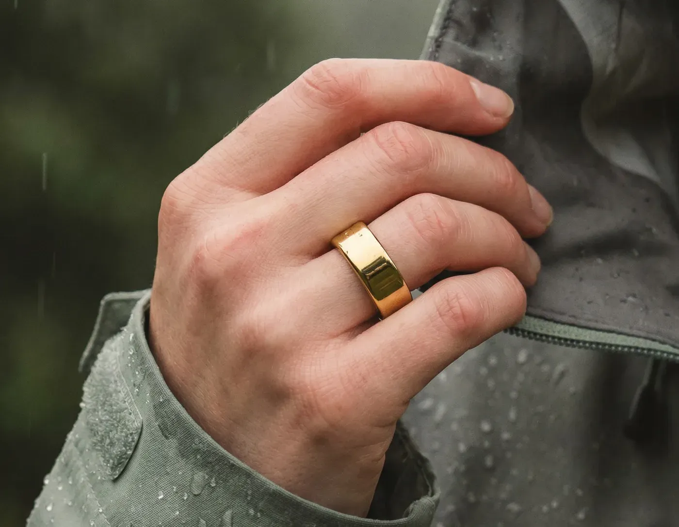 Ultrahuman Ring Pro dorée portée au majeur, main posée sur une veste de pluie mouillée